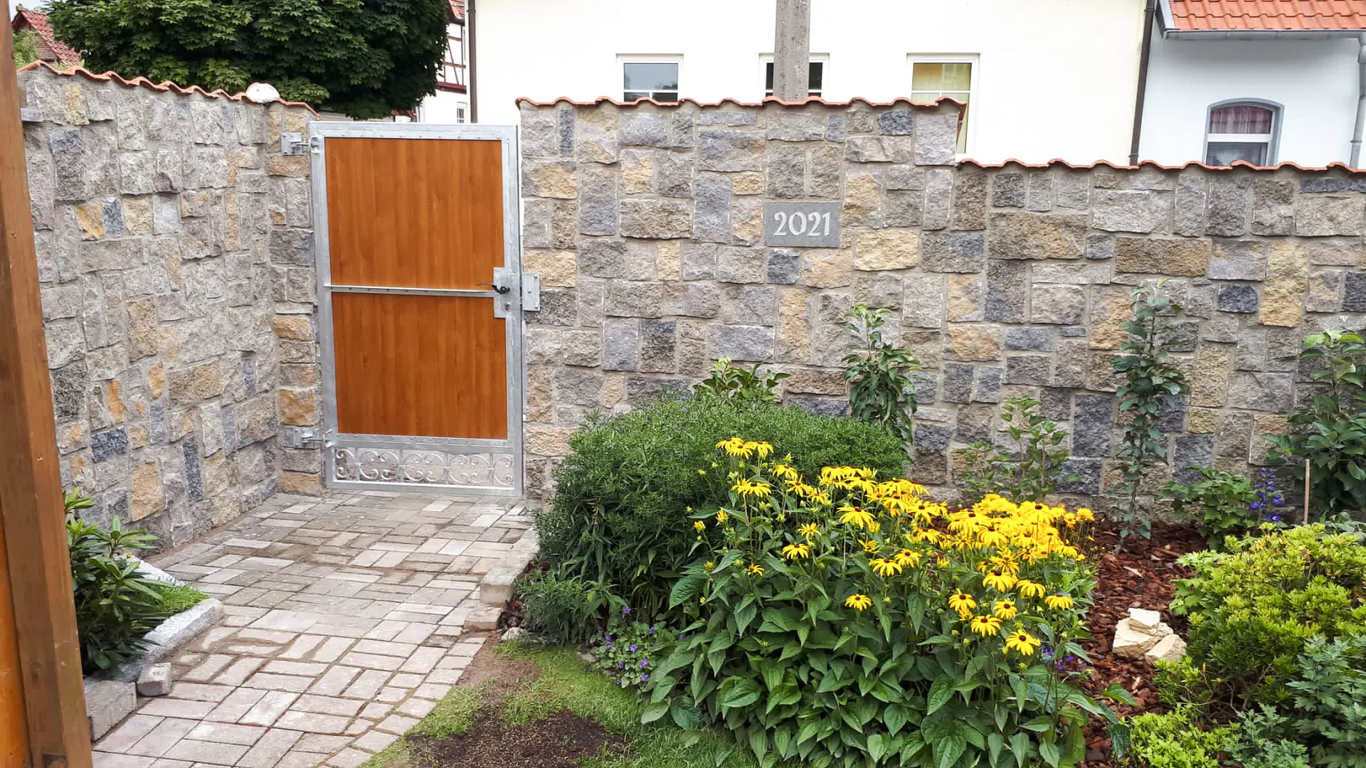 Mit Naturstein veredelte Gartenmauer mit Holztor
