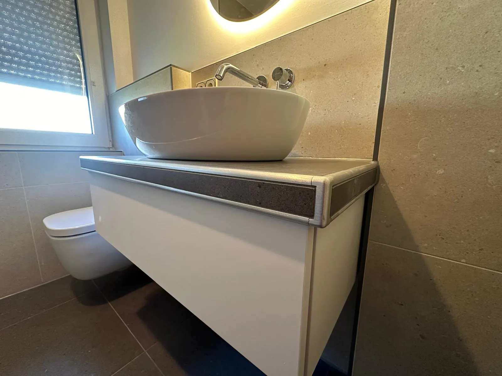 Sanierter Toilettenraum mit Aufsatzwaschbecken und beleuchtetem Spiegel